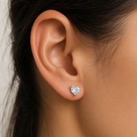 Heart-shaped diamond earring worn by a person with dark hair.