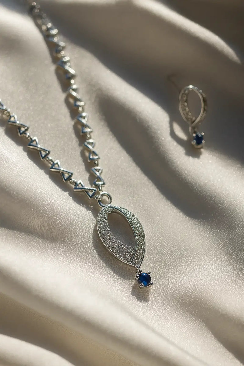 Silver necklace with blue gemstone and matching earring on a beige fabric background